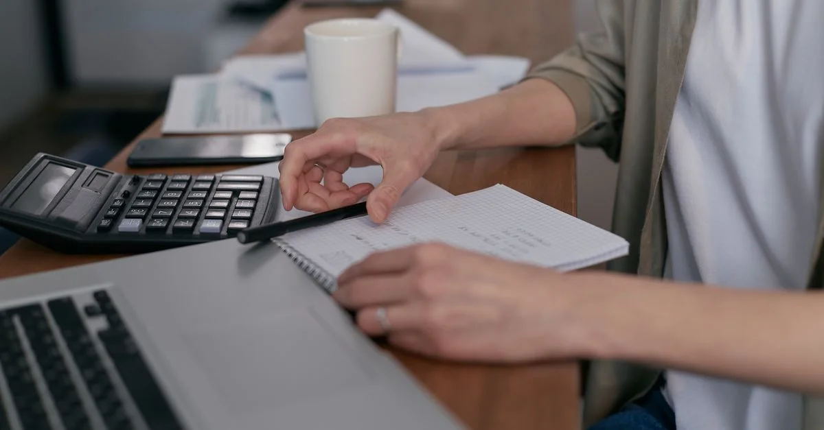 Un adulte d'âge moyen qui calcule ses finances avec un ordinateur portable et un bloc-notes, gérant les budgets à la maison.