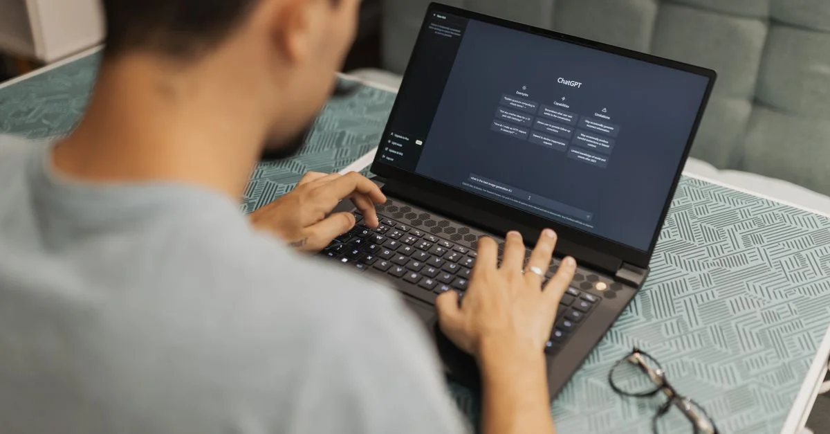 Homme utilisant un ordinateur portable avec une interface AI, tapant avec une attention concentrée. À l'intérieur, portant des lunettes à côté.