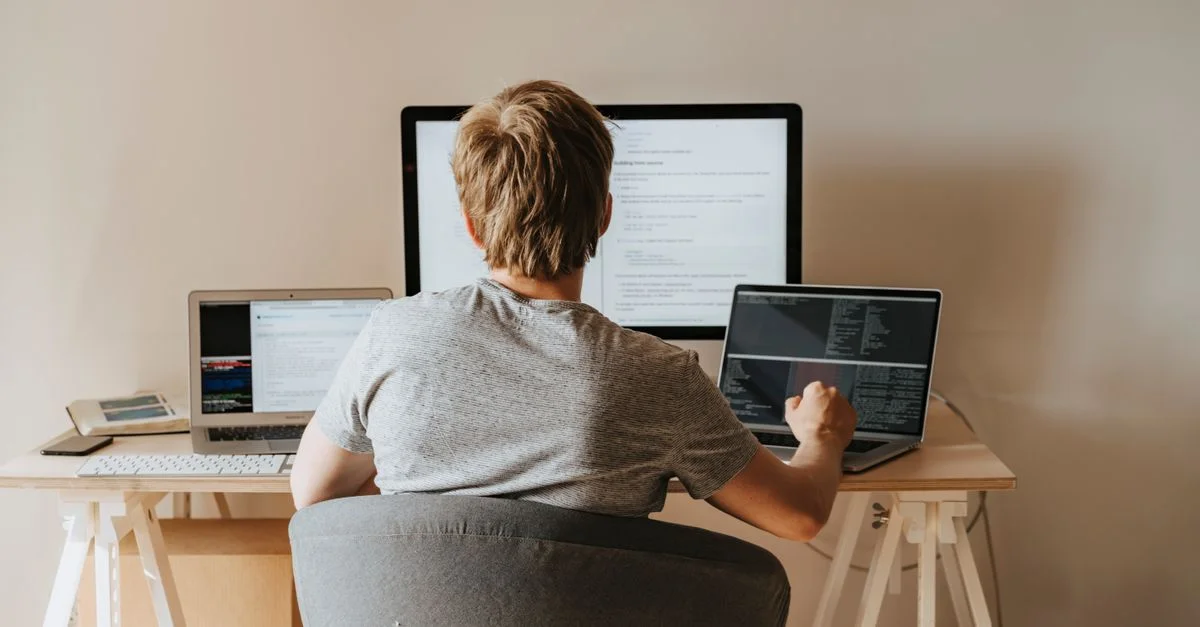 Adolescent programmant avec plusieurs ordinateurs portables dans un espace de travail moderne. Idéal pour les thèmes technologiques et éducatifs.