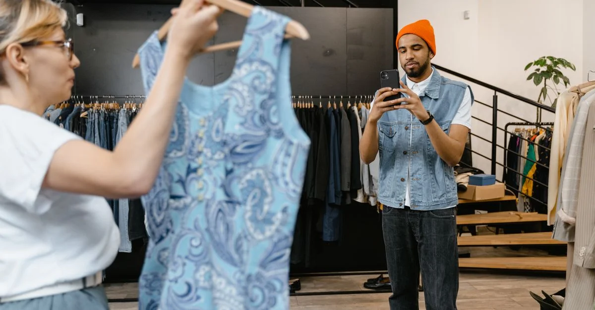 Un jeune homme photographie une robe dans une boutique, se concentrant sur les tendances de la mode.