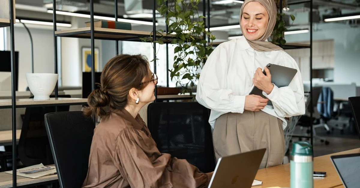 Deux femmes professionnelles dans un cadre de bureau moderne interagissant de manière positive avec des ordinateurs portables.